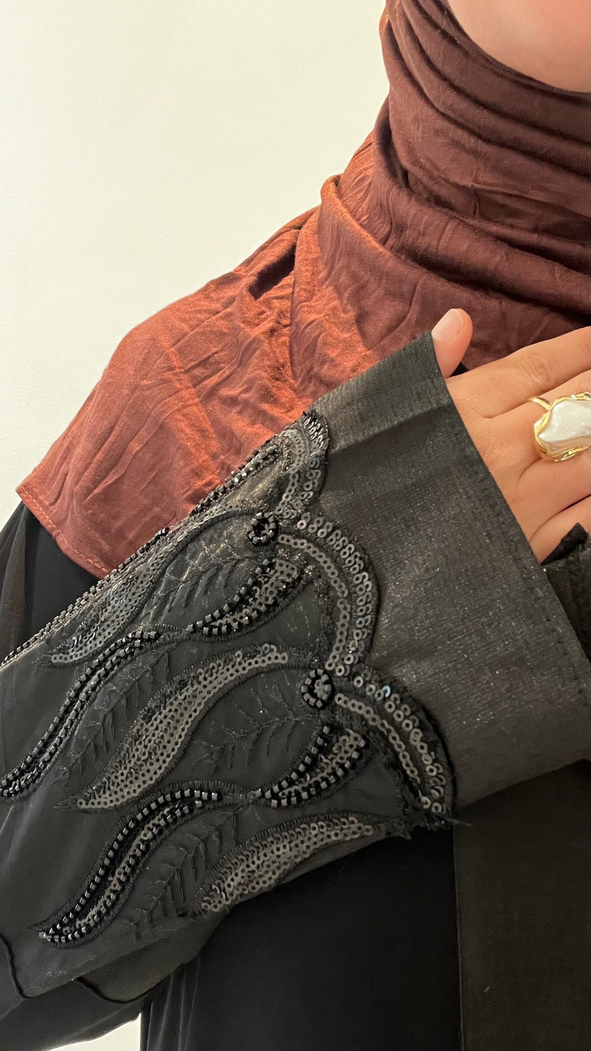Abaya Layl noire - gros plan poignet en broderie perlée, portée avec hijab terracotta